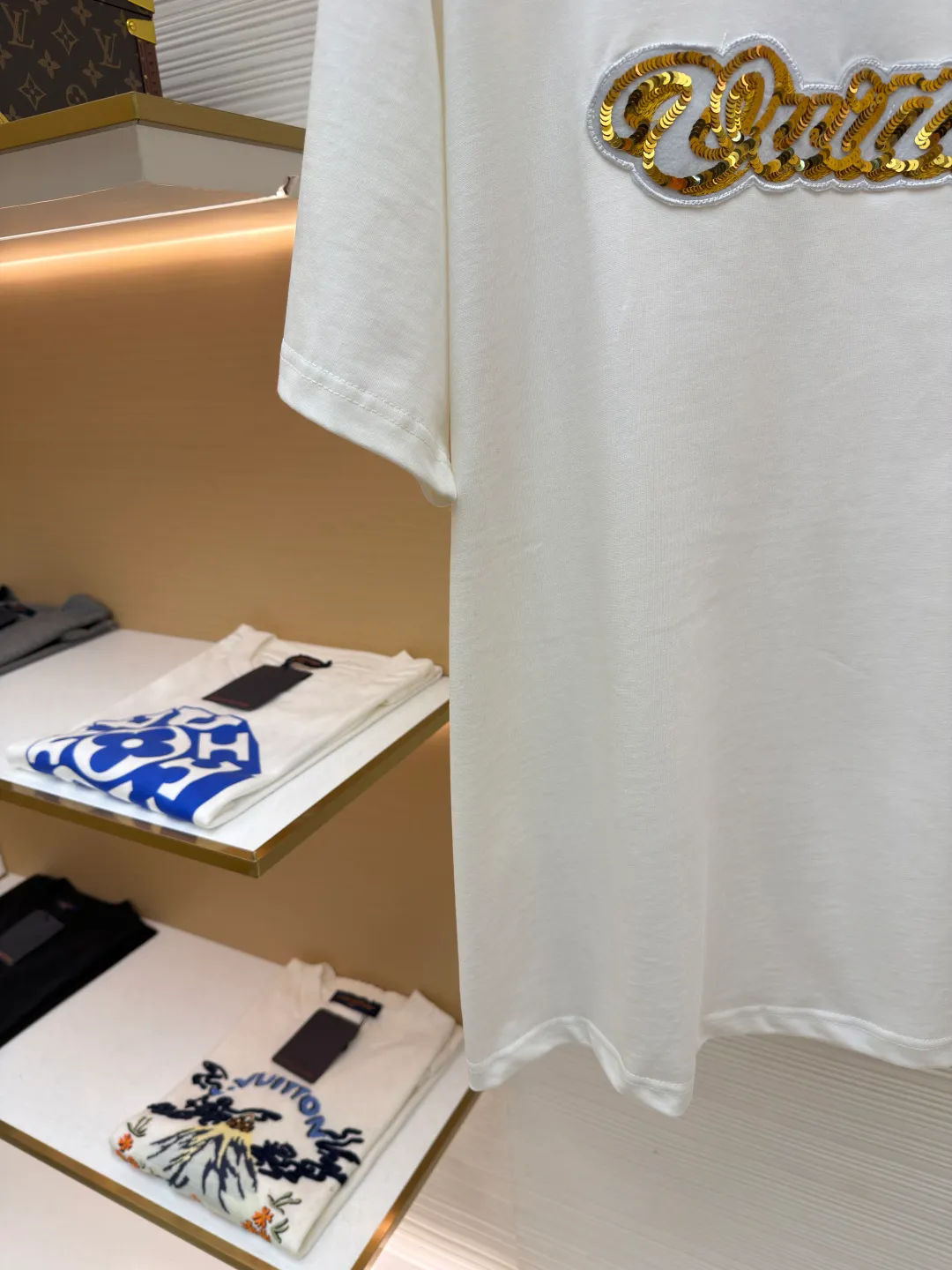 LOUIS VUITTON cotton round neck embroidered Vuitton signature logo short sleeves ●Original version: purchased and developed for 12300 ●Item number: 1682272-A10 ●Fabric: cotton fabric ●Technology: embroidery production ●Color: white ●Version: fitted version ●Weight: about 270 grams ●Size: S-M-L-XL ●Description: This white short-sleeved T-shirt is made of high-count combed cotton fabric and has been treated with pre-washing technology. It has a soft and skin-friendly touch and is not easy to deform. The silhouette of the shirt is a loose shoulder design, which meets the needs of modern casual wear. The core decoration area on the chest uses hand-beading and bronzing technology, and uses metallic gold sequins and embroidery threads intertwined to outline a three-dimensional letter pattern. The sequins are layered and inlaid, and each one is manually positioned and fixed by craftsmen to ensure a regular texture and uniform gloss. The edges of the letters are sewn with matte silk thread to form a visual contrast between gold and matte, while reinforcing the decorative structure to avoid falling off during wear. The neckline uses double-needle hemming technology and is matched with ribbed cuffs of the same fabric. It is durable and fits the neck. The overall craftsmanship combines handicraftsmanship with modern clothing technology, and the details show exquisite texture. The overall wiring is straight and delicate, the fabric is comfortable and soft, and the color is consistent without color difference. It can be matched with the same style to create a fashionable look and control various occasions. Customized accessories, complete with three standards, same style for men and women!
